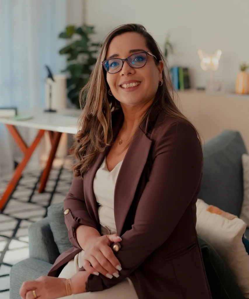 Ary Aguilar sorrindo, sentada em um ambiente de trabalho.